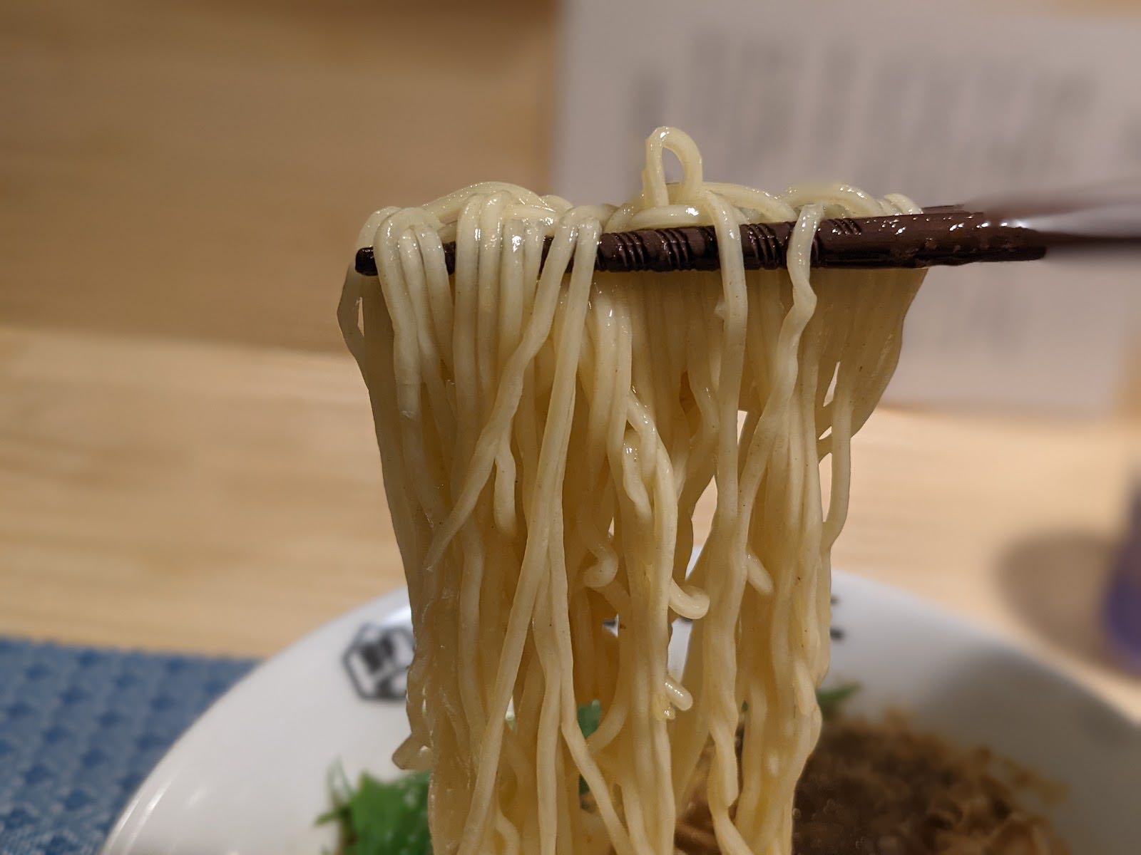 箸で持ち上げた自家製麺。下に鯖そばの丼が見えている。