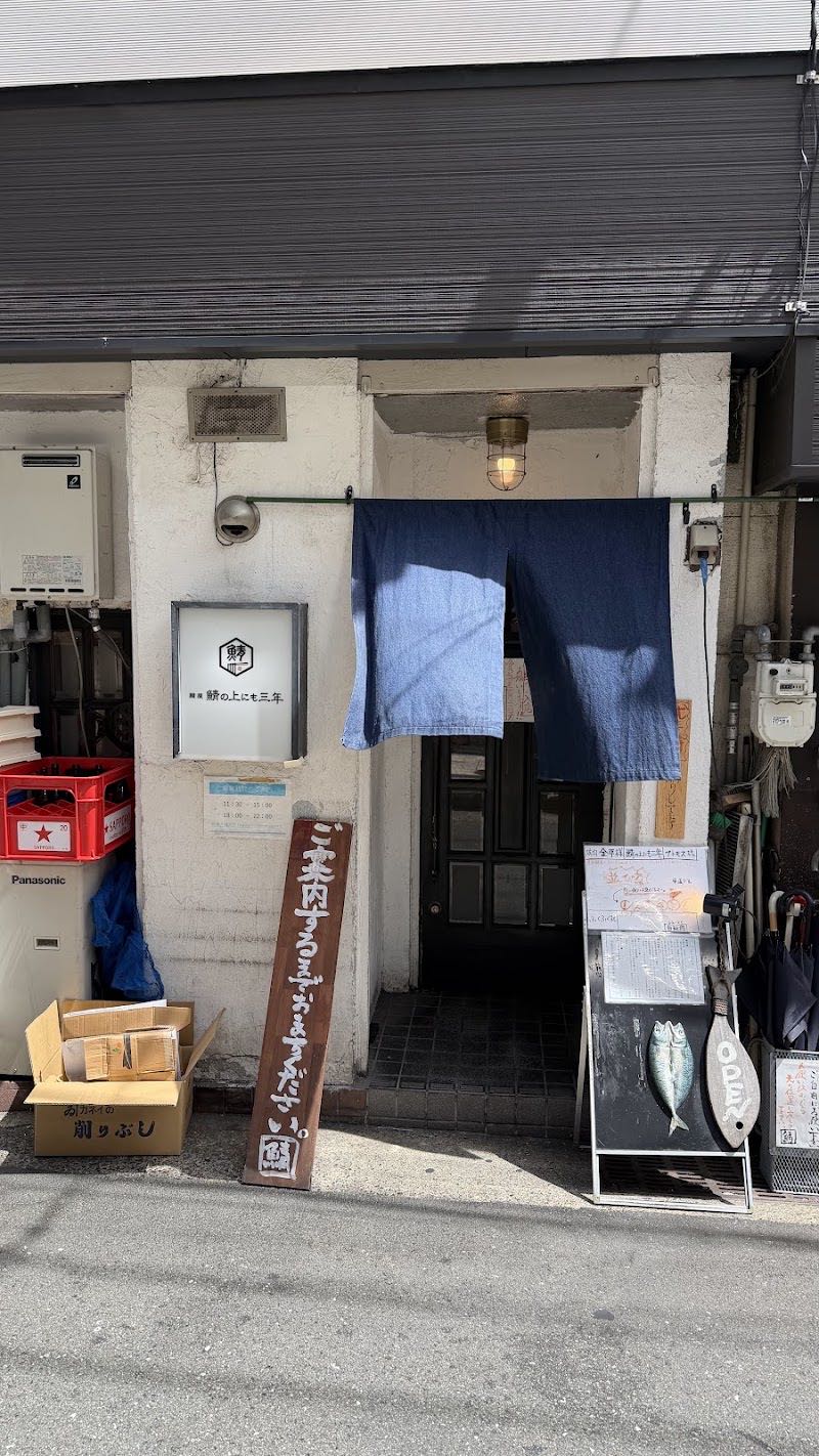 お店の外観。白壁に「麺屋 鯖の上にも三年」の看板、藍色の暖簾、鯖の絵の黒板。