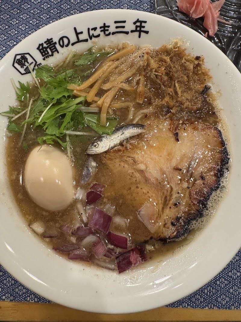 鯖そば。焼いた鯖の身とチャーシュー、味玉、水菜。丼のふちに「鯖の上にも三年」と店名が入っている。